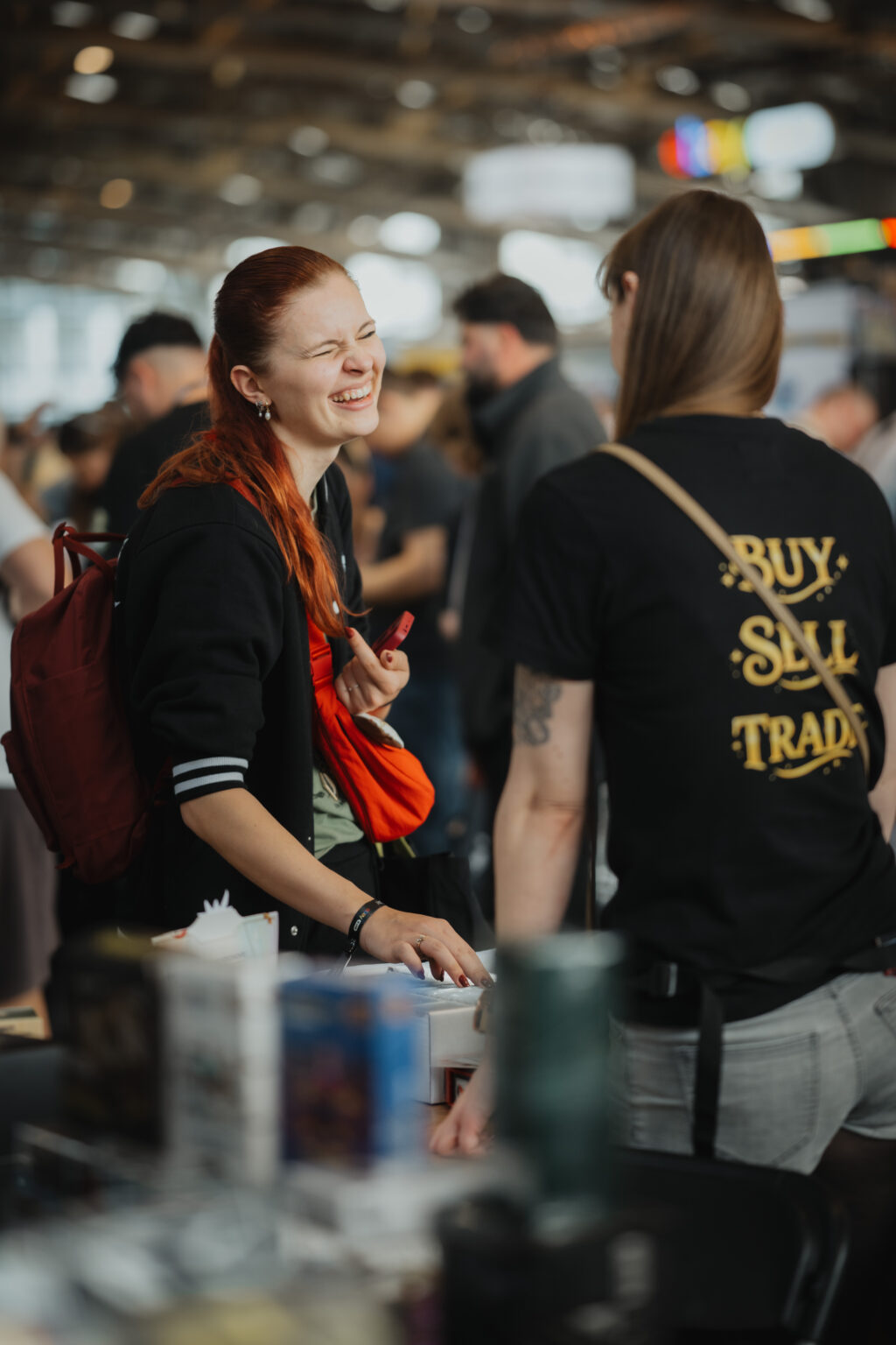 Two visitors browsing cards at a buy, sell and trade booth at CARDMADNESS