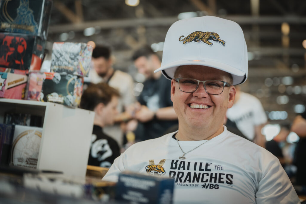 Smiling visitor in a white cap in front of a trading card booth at CARDMADNESS